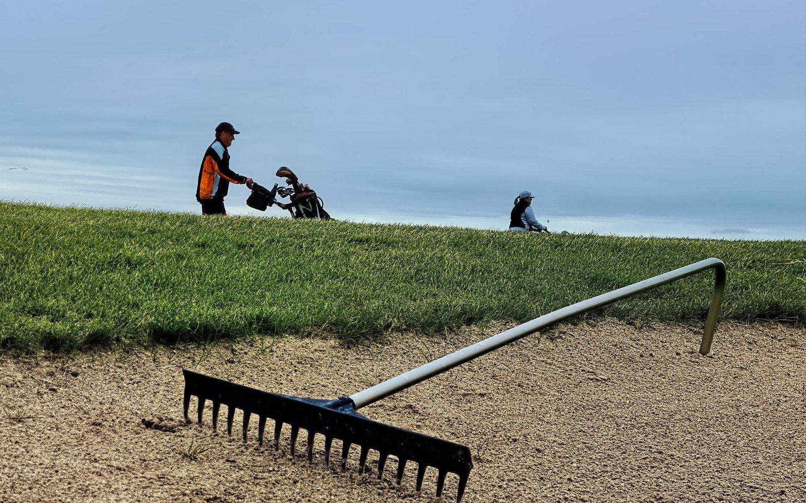 Adult greenkeeper's hands cutting and placing revetted turf courses on a bunker face, tools and cut sods visible, close framing