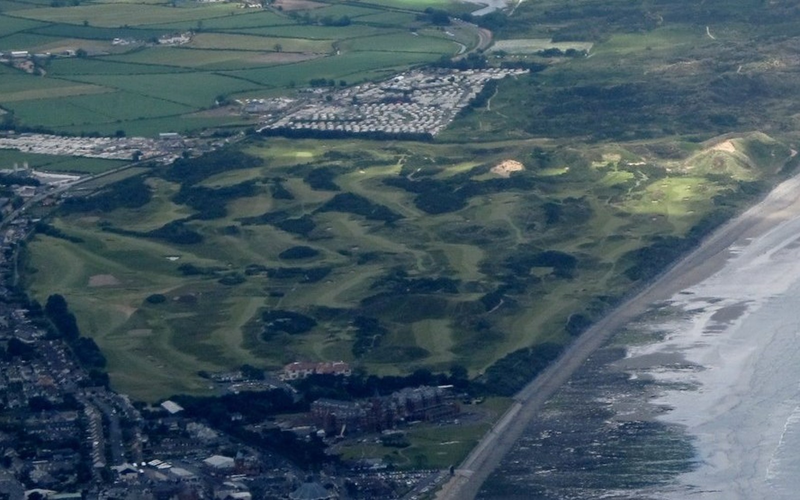 Aerial view of a coastal links golf course beside a beach and caravan park