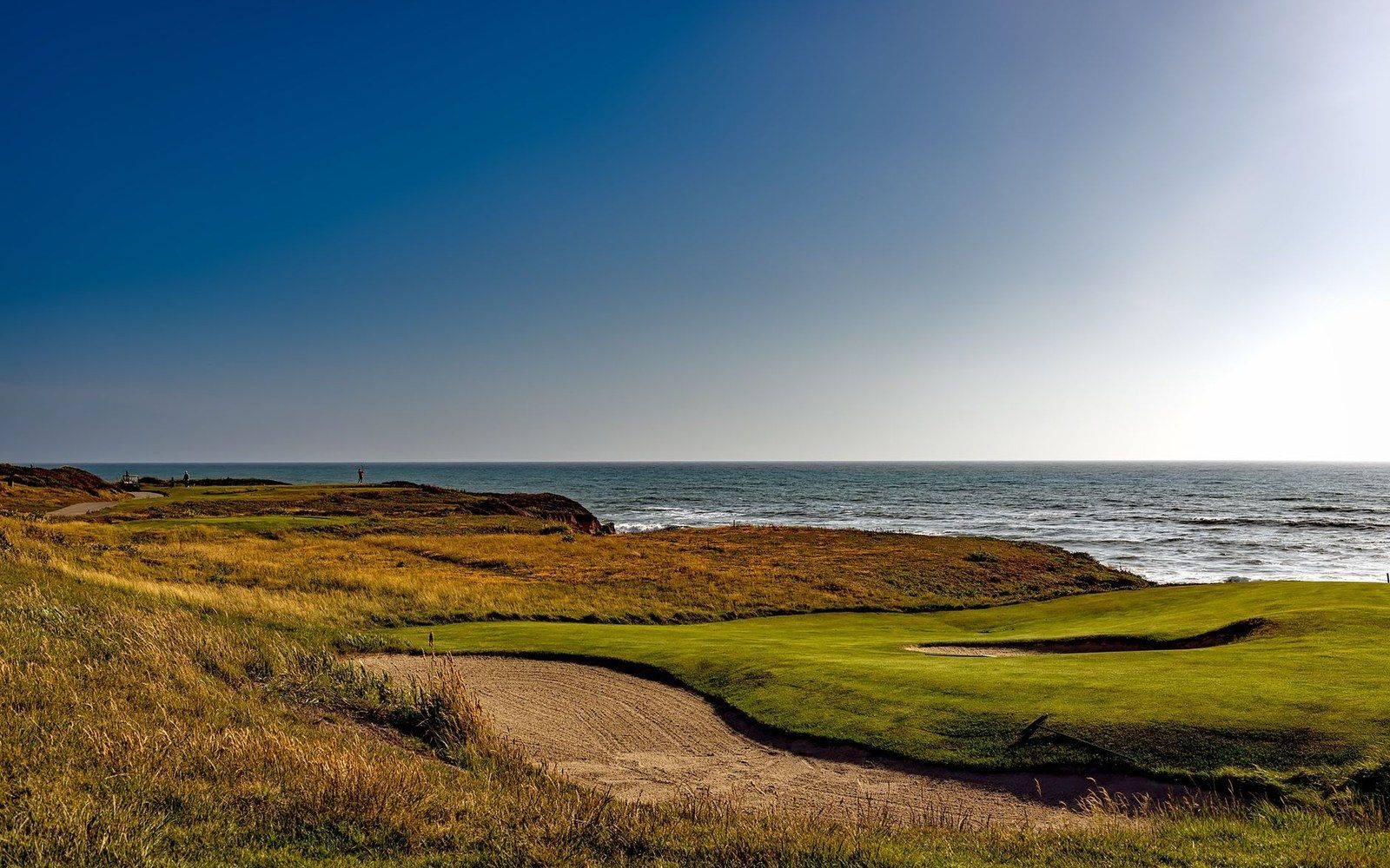 Golf course green with sand bunker sits along a coastal cliff edge above the ocean