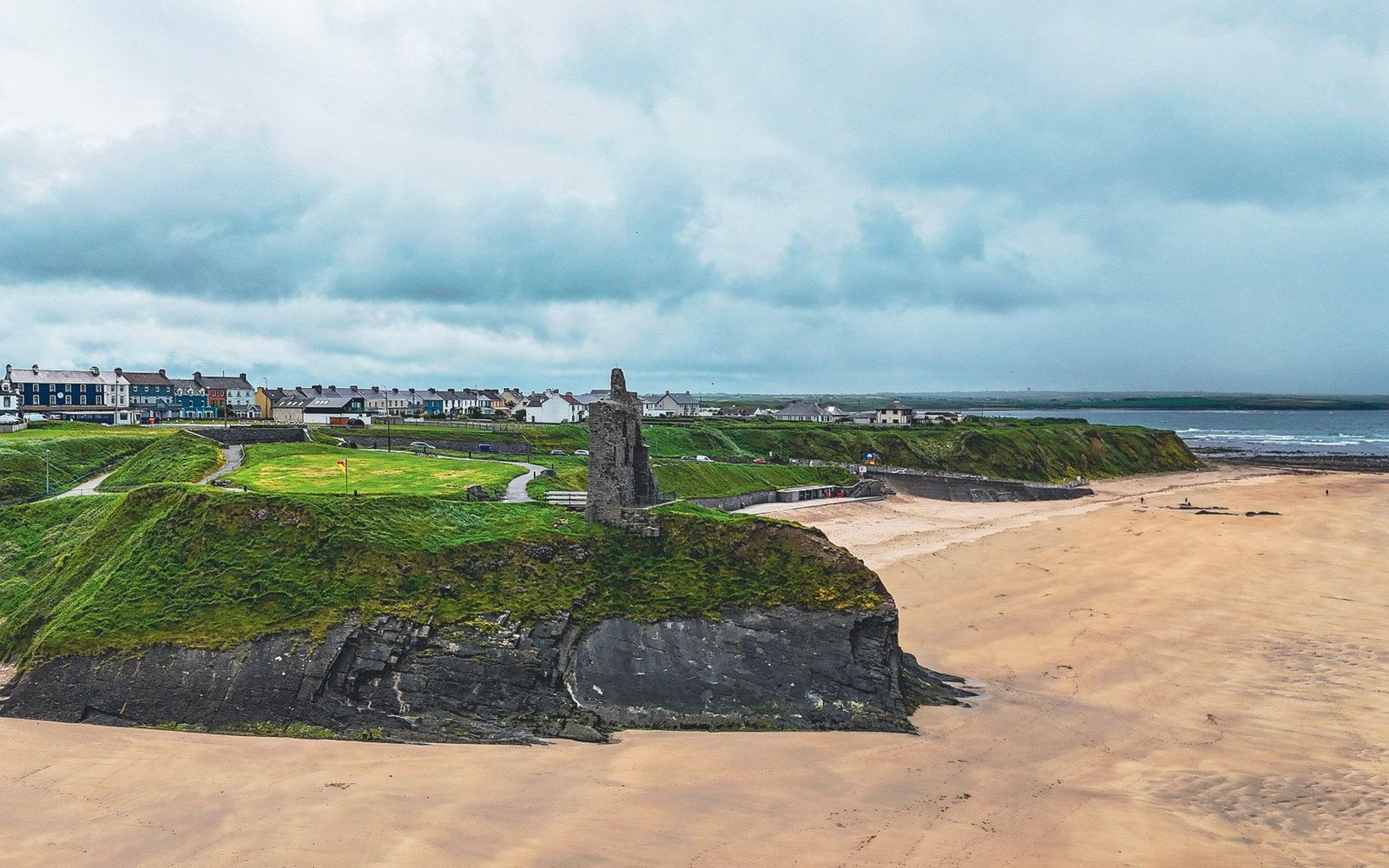 Ruined castle tower on a grassy clifftop above a wide sandy beach