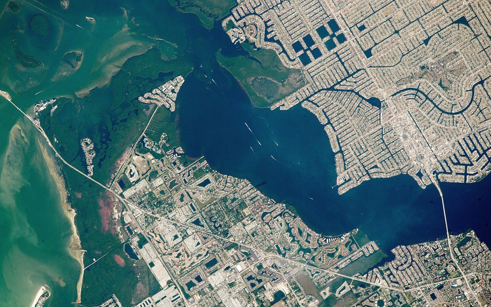 Satellite view of a coastal bay with canal-lined suburban developments and barrier islands