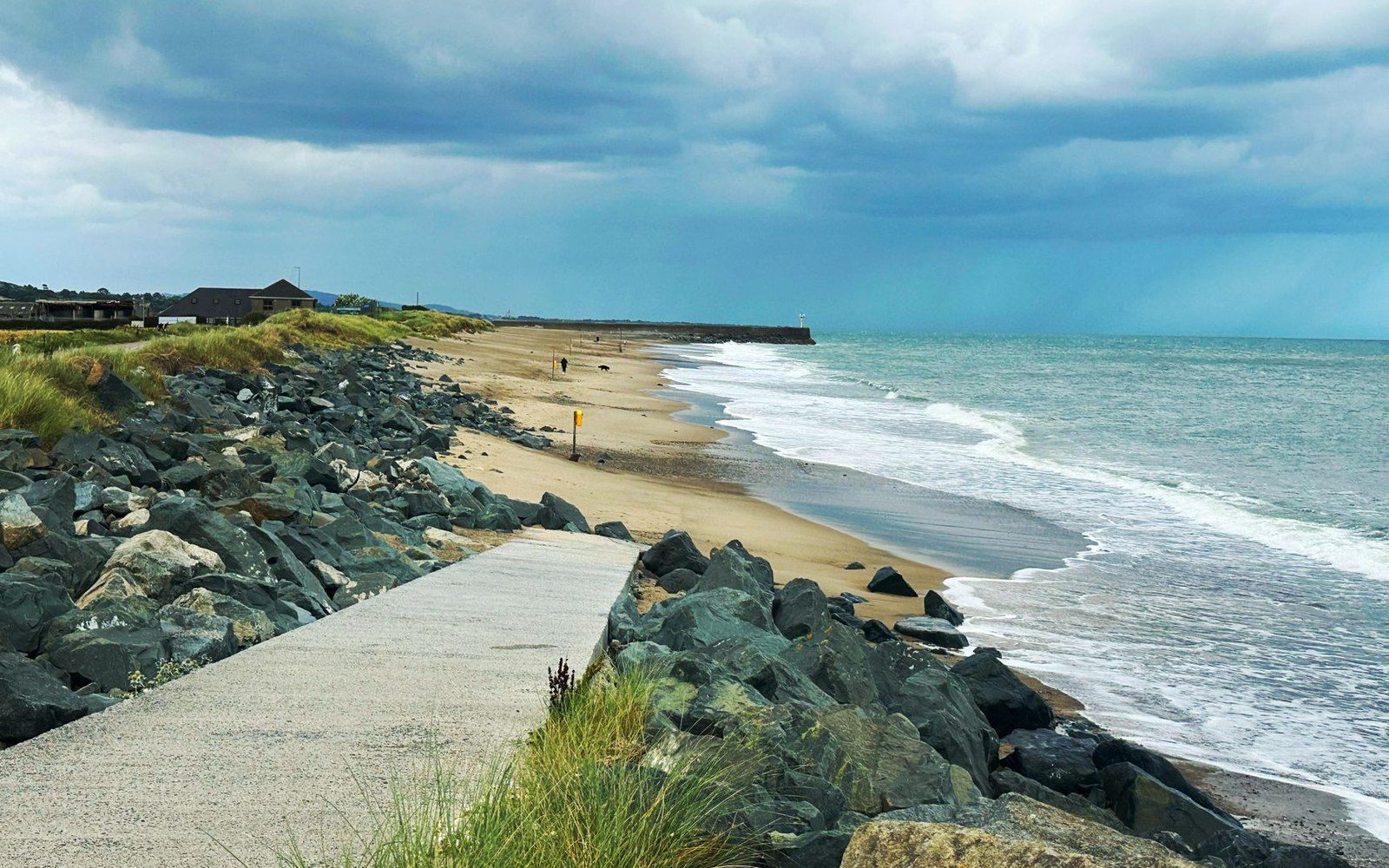 Rocky sea wall lines a sandy beach beneath a cloudy sky