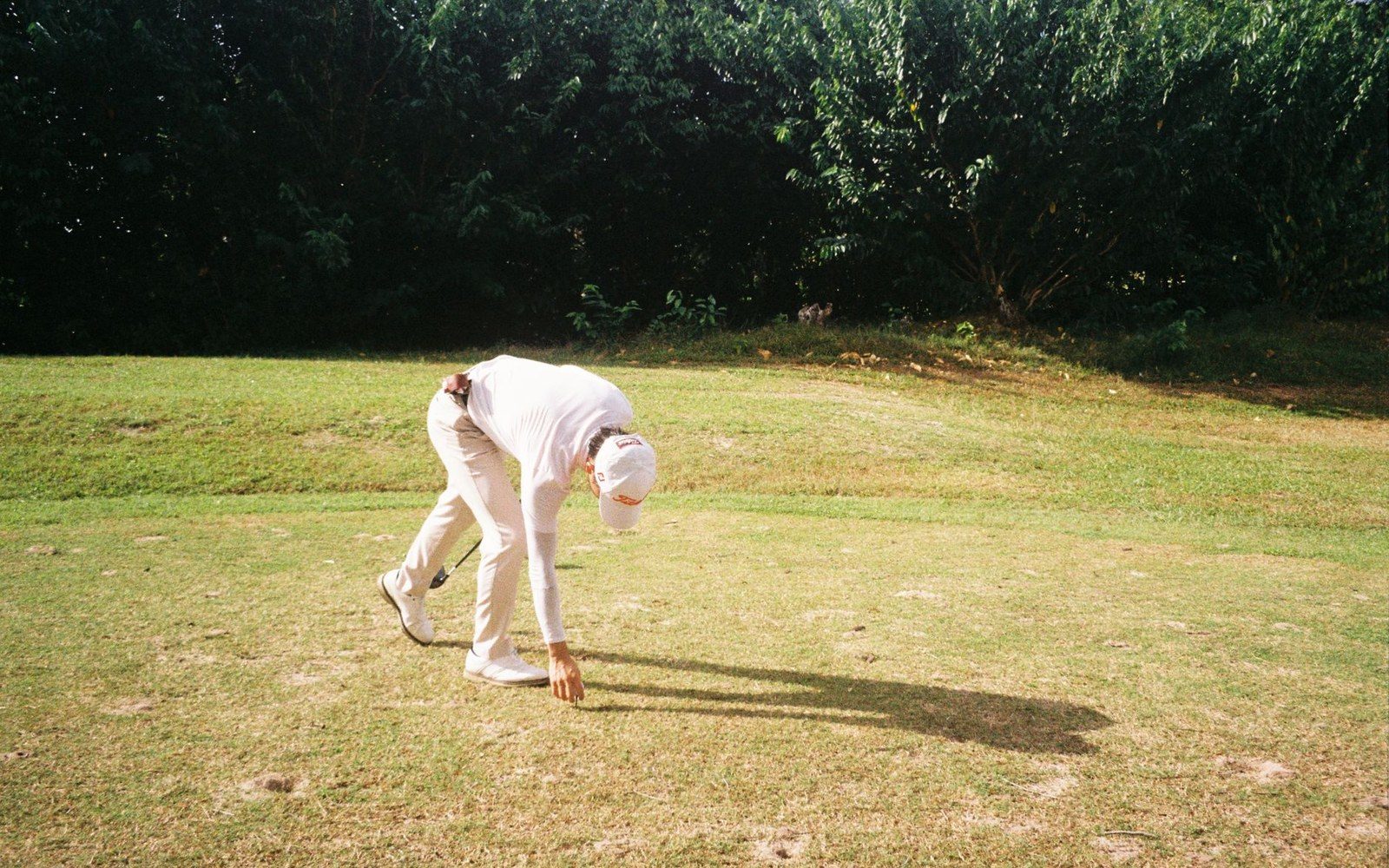 Golfer bends down to pick up a ball on a sunlit fairway