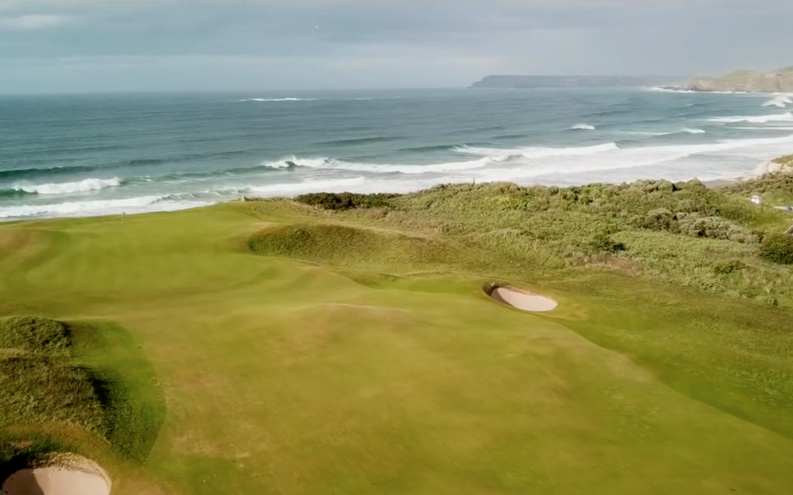 Coastal links golf course with sand bunkers overlooking waves crashing on the shore