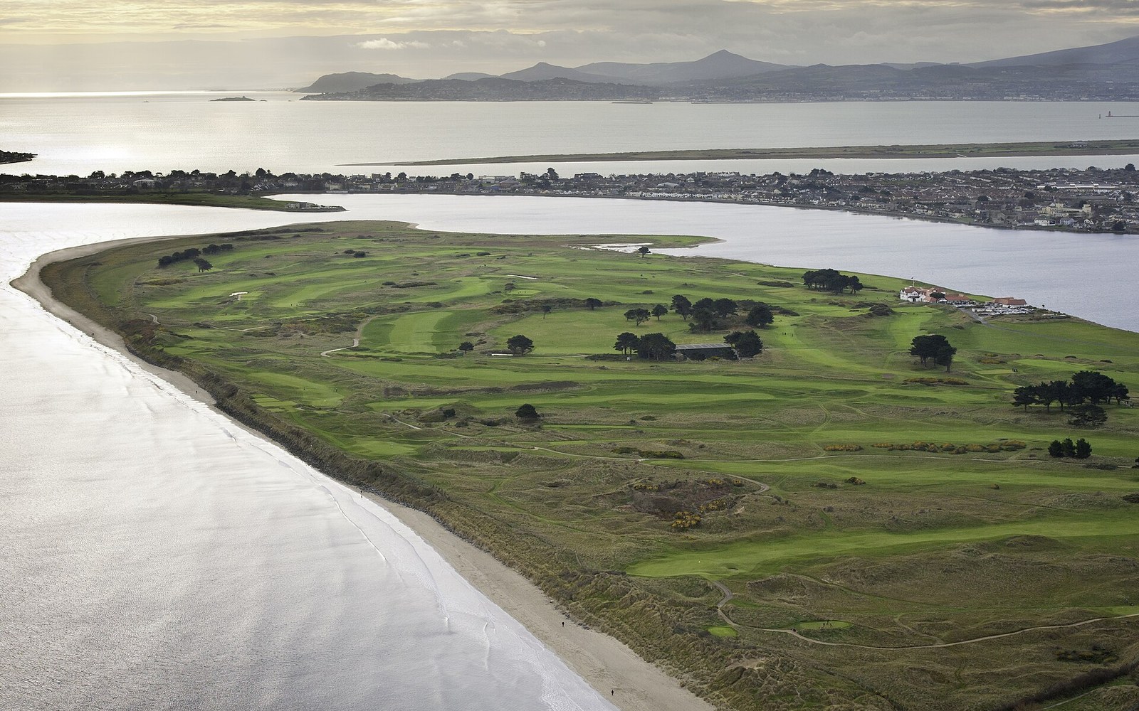 Aerial view of a coastal golf links on a narrow sandy peninsula near a bay