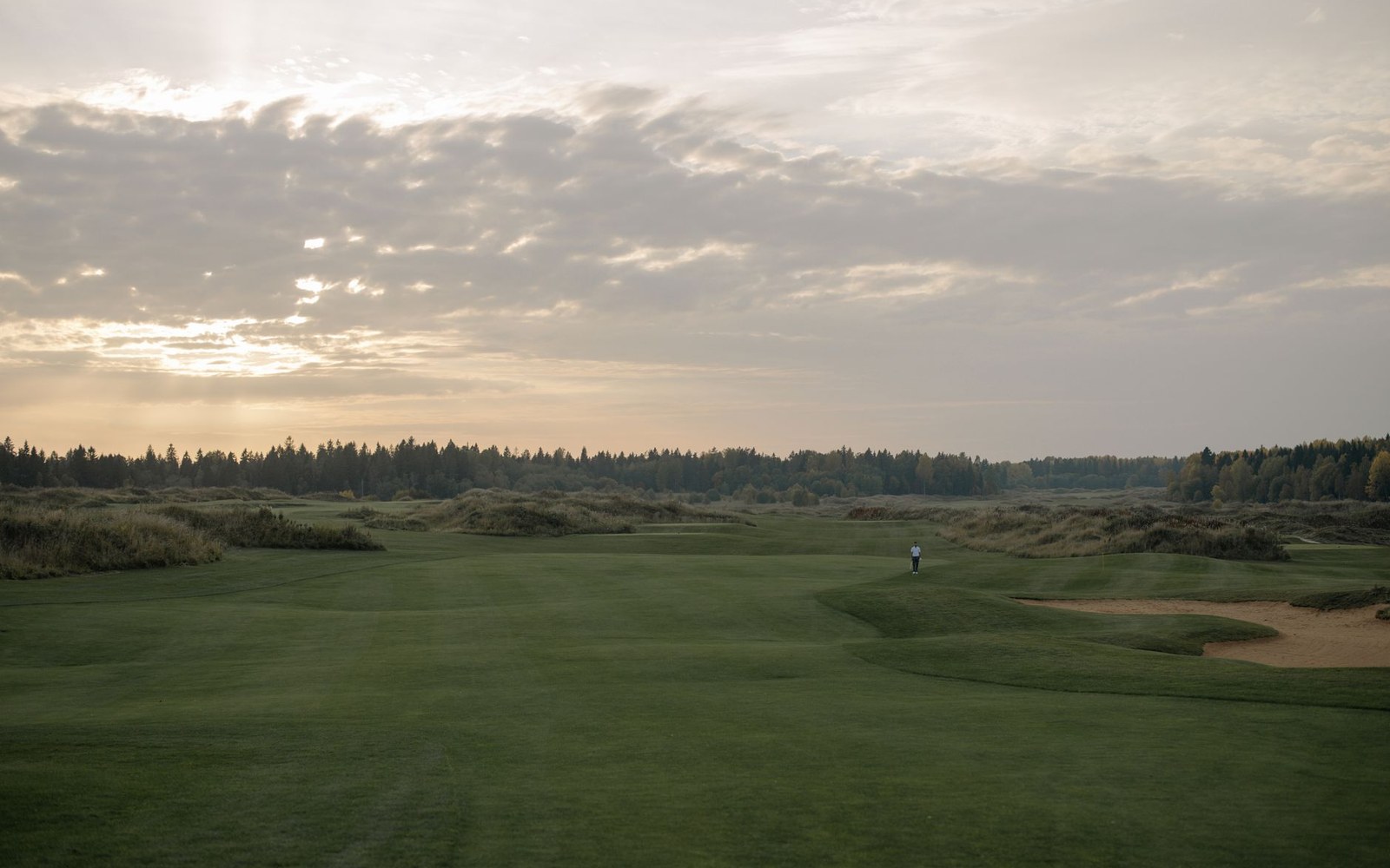 Golf course fairway with sand bunker under a cloudy dawn sky lined by trees