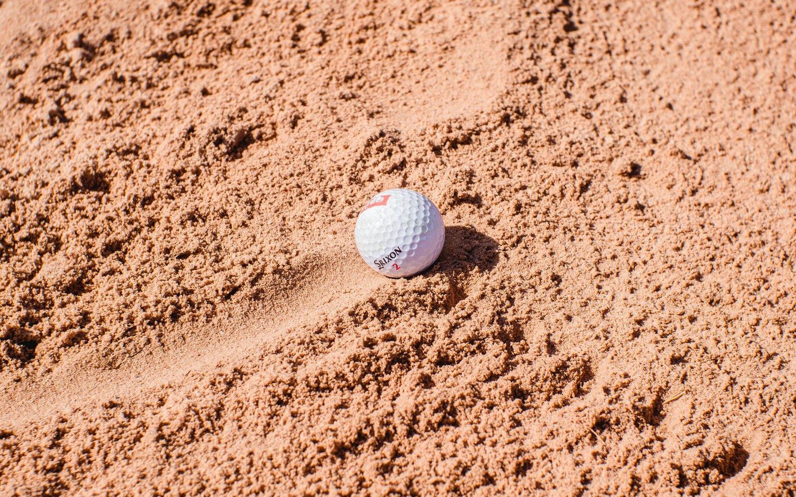 A golf ball resting in a sand bunker on a golf course