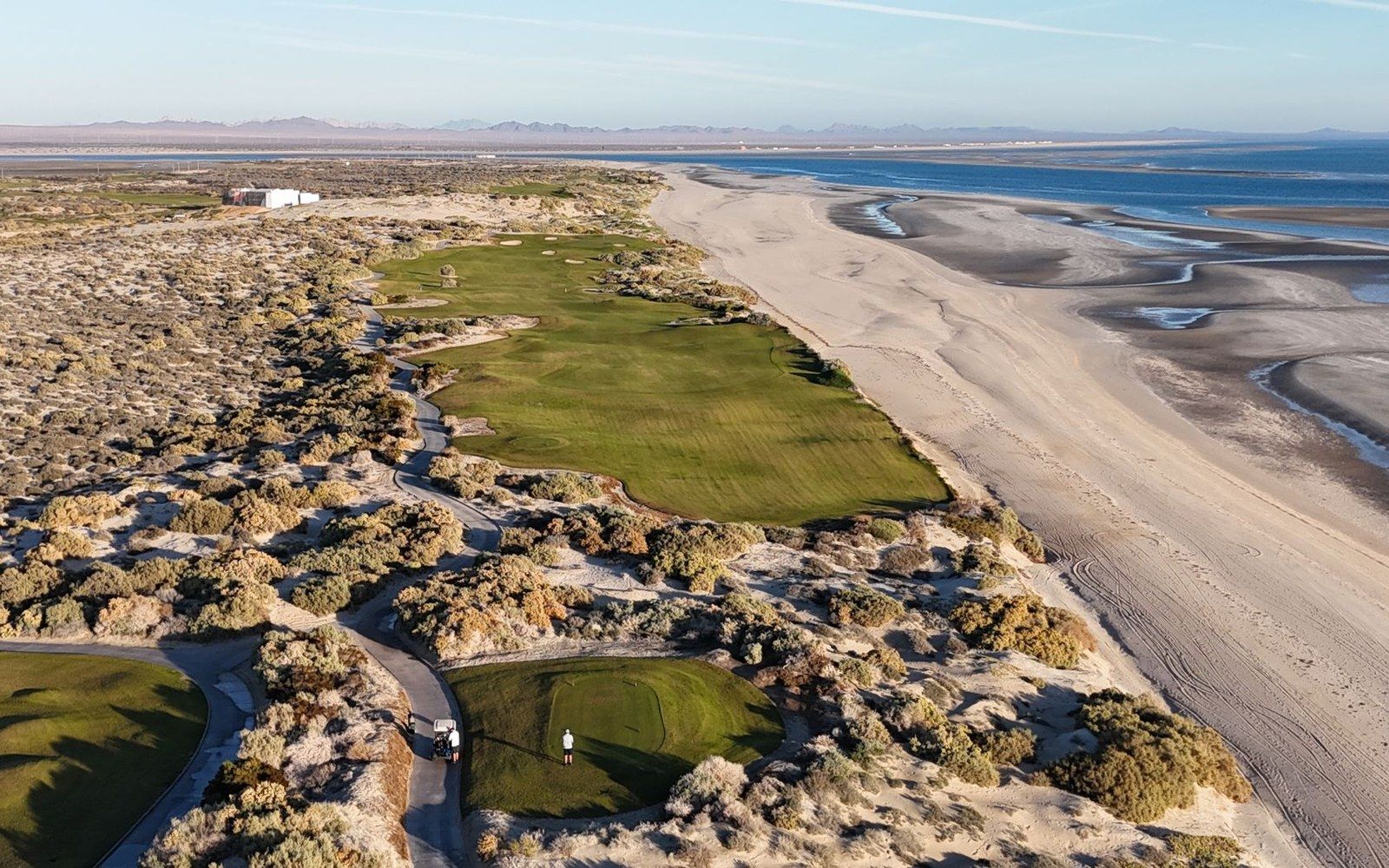 Aerial view of a coastal golf course fairway and green bordered by desert scrub and beach