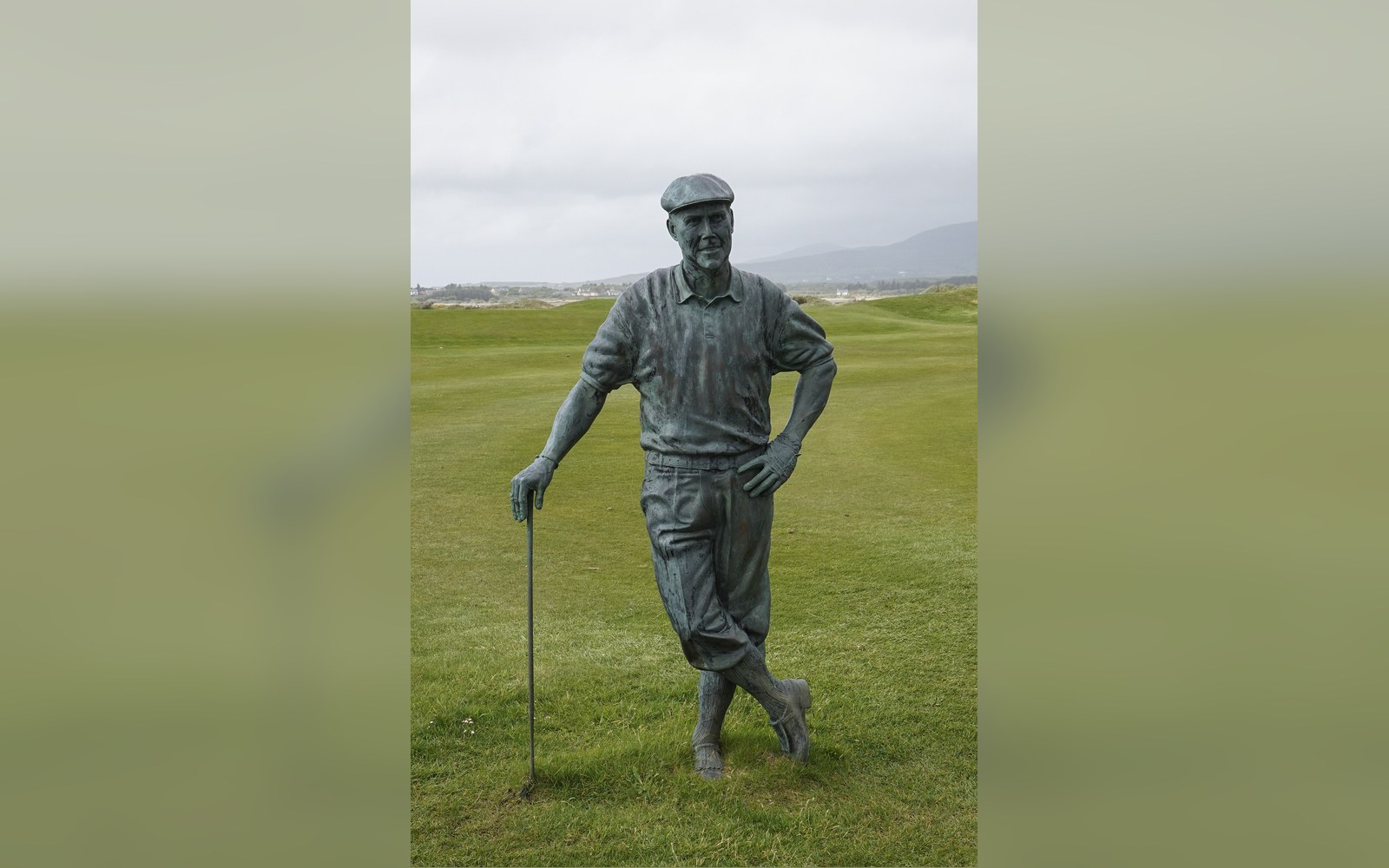 Bronze statue of a golfer leaning on a club beside a links course
