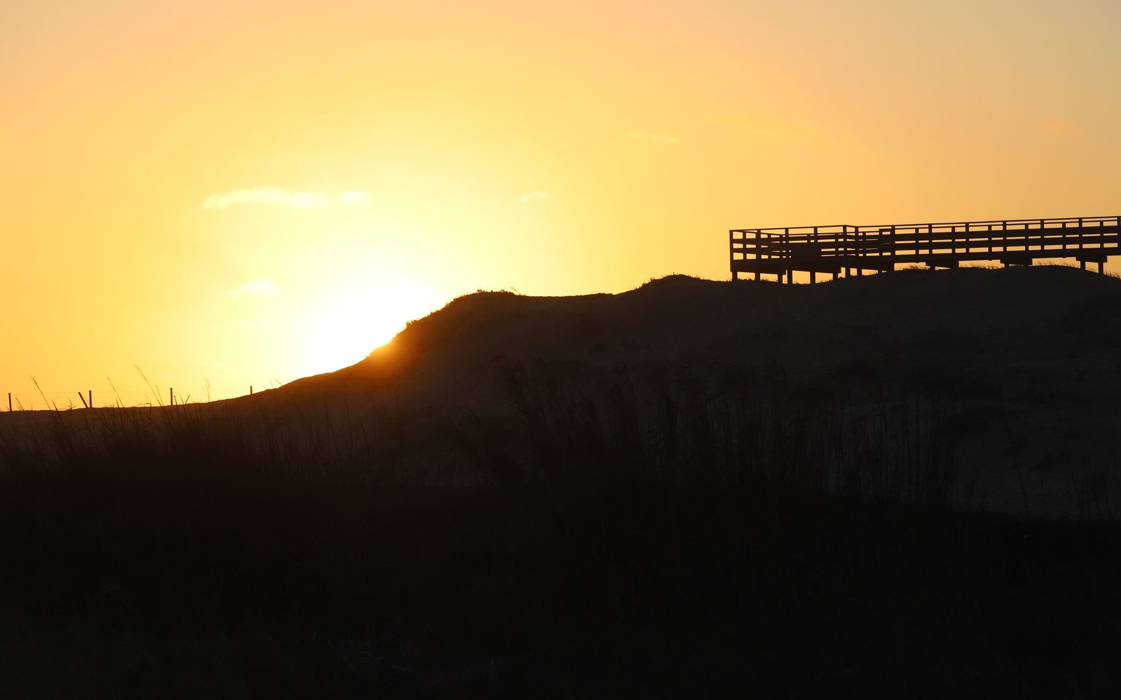 Sun setting behind a dune with a wooden viewing platform silhouetted on top