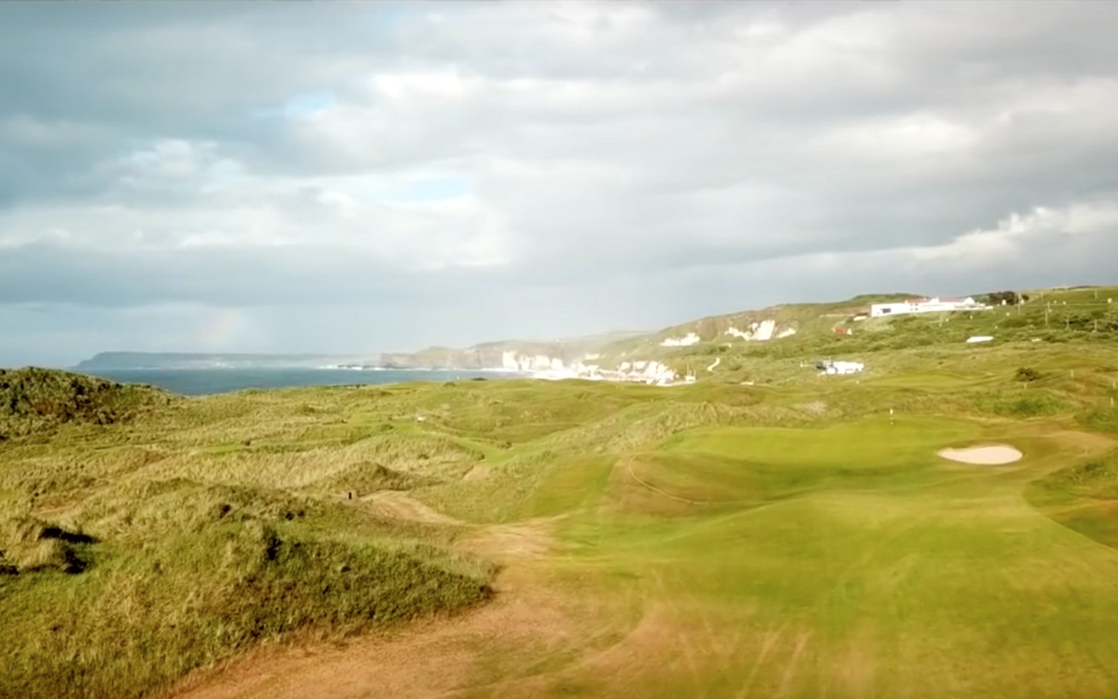 Rock armour laid against the dune line at Royal Portrush, course boundary fence visible above it, overcast sky